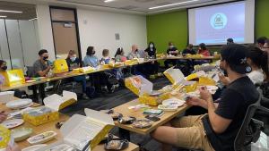 People in classroom sitting at tables with boxes of food