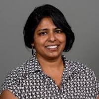 Indulata Prasad wearing patterned shirt smiling